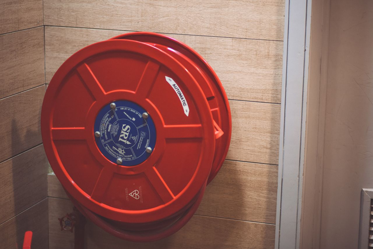 A red fire hose reel mounted on a wooden wall indoors for safety.